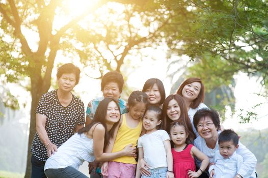 Large group of Asian multi generations family portrait, grandparent, parent and children, outdoor nature park in morning with sun flare.