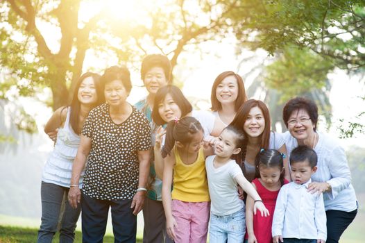 Large group of cheerful Asian multi generations family portrait, grandparent, parent and children, outdoor nature park in morning with sun flare.