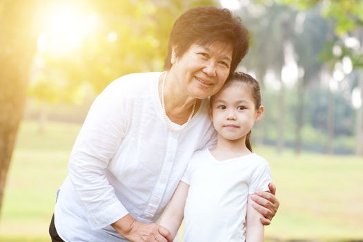Portrait of beautiful multi generations Asian family at nature park. Grandmother and granddaughter at outdoor. Morning sun flare background.