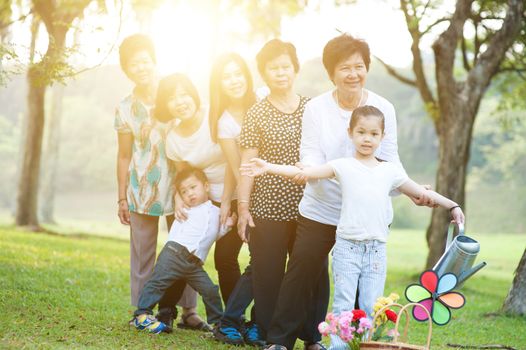 Large group of happy Asian multi generations family playing at park, grandparent, parent and children, outdoor nature park in morning with sun flare.
