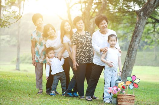 Large group of Asian multi generations family playing at park, grandparent, parent and children, outdoor nature park in morning with sun flare.