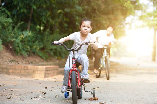 Portrait of active multi generations Asian family at nature park. Grandmother and granddaughter cycling outdoor. Morning sun flare background.