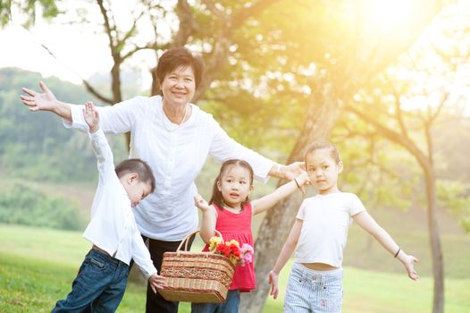 Portrait of beautiful multi generations Asian family at nature park. Grandmother and grandchildren having fun at outdoor. Morning sun flare background.