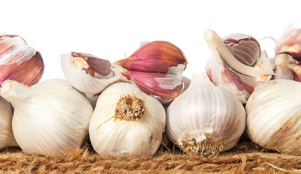 Pile of whole and cloves of garlic on sackcloth isolated on white background