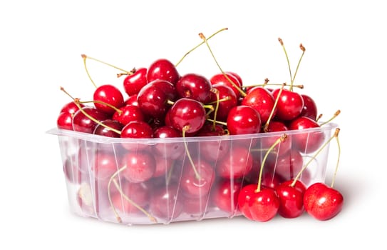 Red sweet cherries in plastic tray rotated and three near isolated on white background