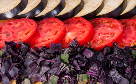 Sliced eggplant tomato and basil leaves horizontally isolated on white background