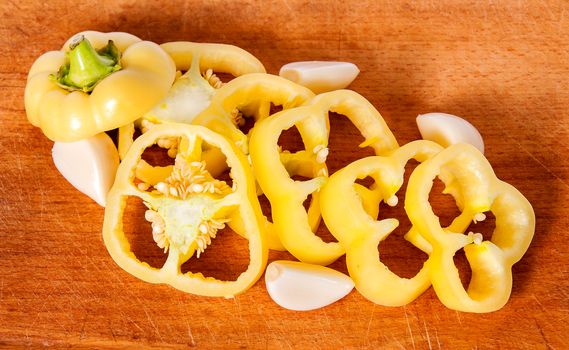 Sliced yellow pepper and garlic cloves on a wooden board