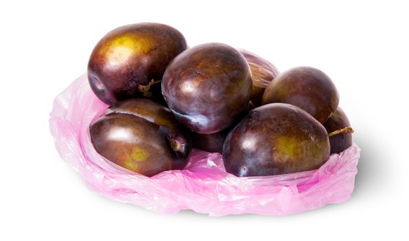 Whole violet plums in plastic bag isolated on white background