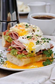 poached  eggs with avocado, tomatoes, slices of ham on a baguette for breakfast