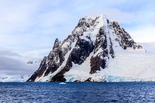 Big stone cliff covered with snow and sea in foreground, close to Argentine islands, Antarctica