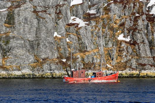 Lone fishing boat floating near steep cliff, Nuuk fjord, Greenland
