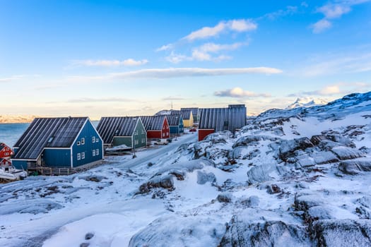 Yellow, blue, red and green inuit houses along the snow street with rocky landscape in foreground and mountain in background, Nuuk city, Greenland