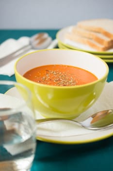 tomato soup in a bowl with toast in a background