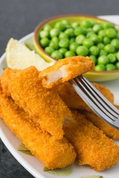 Breaded and Baked Fish Sticks, fingers  on a plate with a bowl of peas and a slice of lemon
