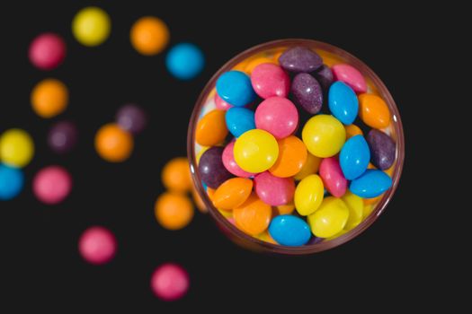 smarties in jar spilling our, on black background