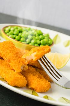 Breaded and Baked Fish Sticks, fingers  on a plate with a bowl of peas and a slice of lemon