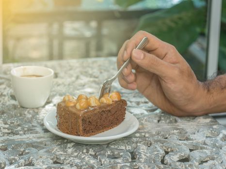 Hand man holding spoon to scoop a piece of cake with a cup of coffe on table