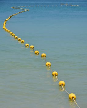 Chain of yellow polystyrene sea marker buoys with cable tow in blue sea water, in perspective