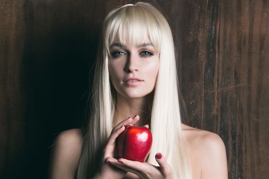 Young pretty blonde woman with long hair holding red apple on wooden background