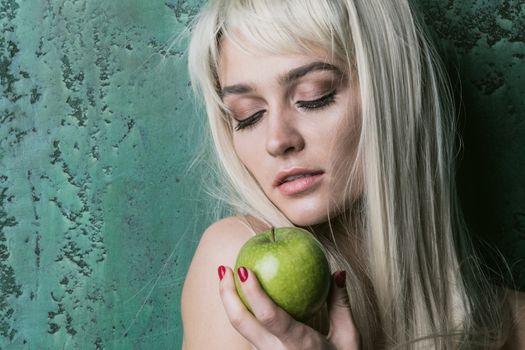 Young pretty blonde woman with long hair holding green apple