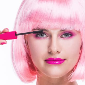 Portrait of girl with glamour make-up and pink hair using mascara isolated on white background