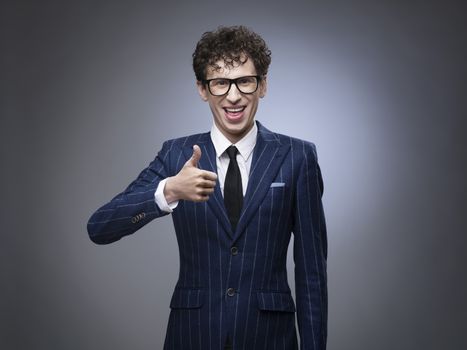 Funny man in striped suit showing thumbs up over gray background. Professional actor facial expression.