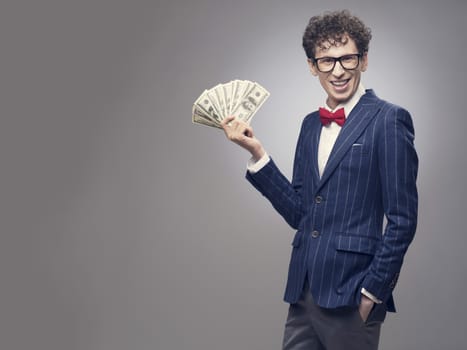 Happy smiling man in a suit holding fan of dollar banknotes on gray background