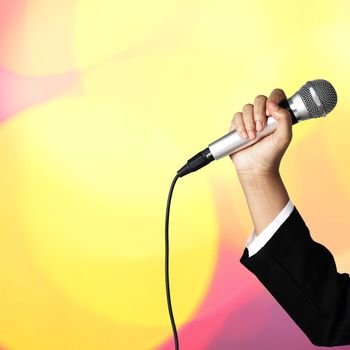 Businesswoman hand holding a microphone on blur of colorful bokeh background, seminar concept.