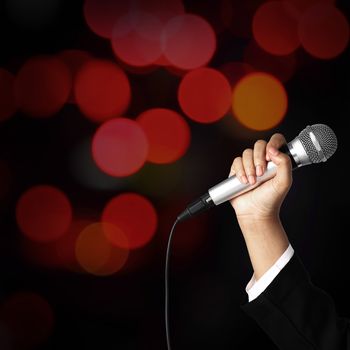 Businesswoman hand holding a microphone on blur of colorful bokeh background, seminar concept.