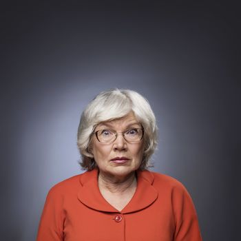 Senior lady staring through her eyeglasses on gray background