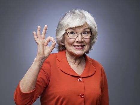 Smiling senior lady showing ok sign on gray background