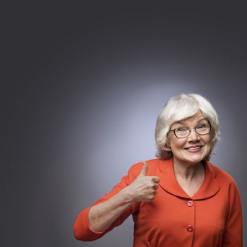 Smiling senior lady showing thumb up sign on gray background with copy space