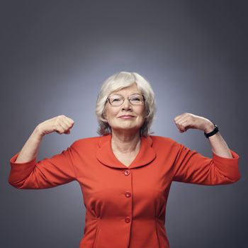 Smiling senior lady showing her muscles on gray background with copy space