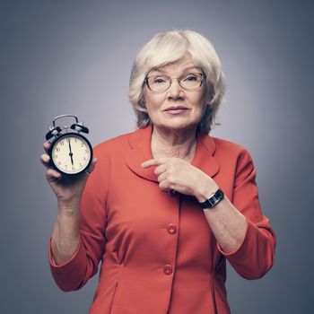 Senior lady pointing to alarm clock showing time of deadline