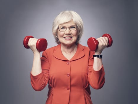 Smiling senior lady with dumbbells on gray background