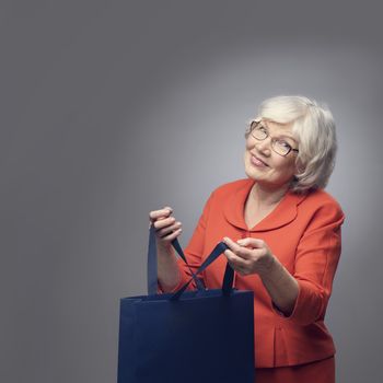 Smiling senior lady with shopping bag on gray background with copy space