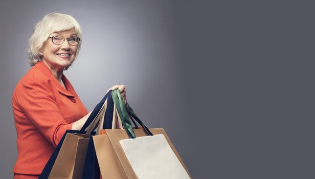 Smiling senior lady with shopping bags on gray background with copy space