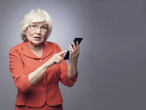 Funny senior lady with smartphone on gray background with copy space