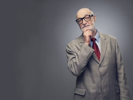 Senior man holding hand on chin and thinking on gray background with copy space