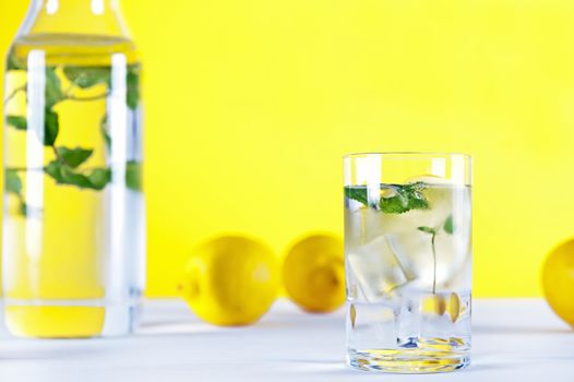 Cold water with lemon and mint on yellow background