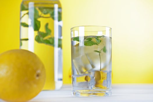 Cold water with lemon and mint on yellow background