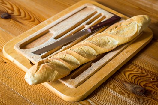 Close up french bread baguette on vintage wooden board with knife