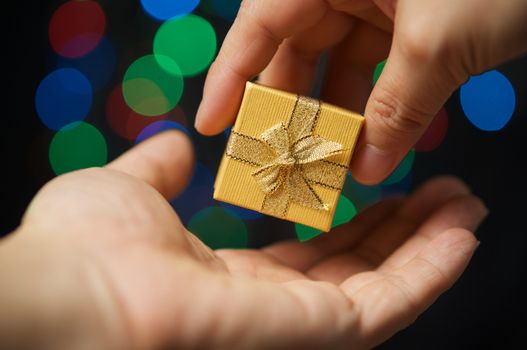 Hand of woman gift present on hand of man have colorful bokeh as background.