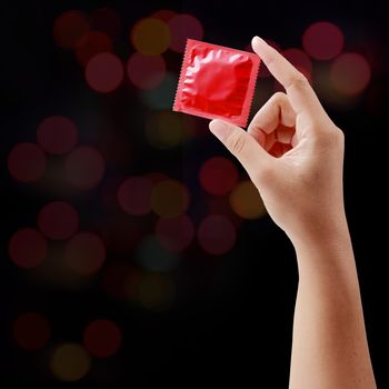 condom in female hand on blurry night light background.

