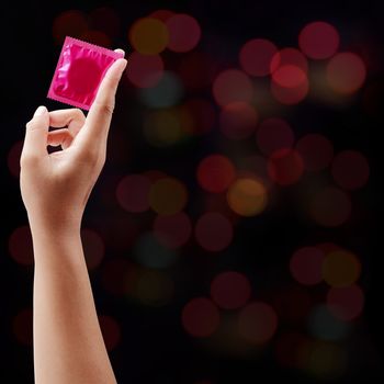 Pink condom in female hand on blurry night light background.
