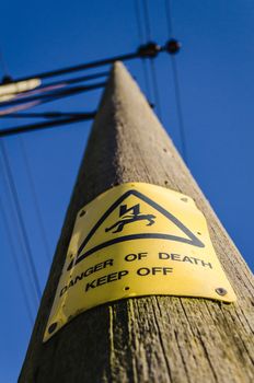 warning yellow electrocution sign on electrical pole against blue sky