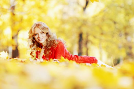 Beautiful young woman laying on yellow leaves in autumn park