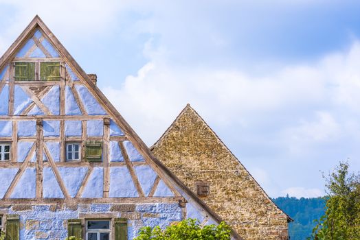 Architectural details from two medieval German houses , one with blue half timbered walls, small windows, wooden shutters and one with aged  stone wall and a single wooden window.