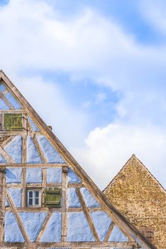 Medieval architecture background with two german gable roofs, one house with blue half timbered walls and one with aged stone wall.