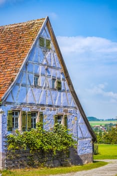 Antique house with German specific architecture, half timbered and stone walls of blue color, windows with wooden shutters and tile gable roof.